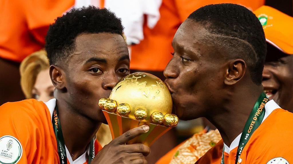 Ivory Coast's Max-Alain Gradel Simon Adingra kiss the Africa Cup of Nations trophy after winning the tournament in 2024.