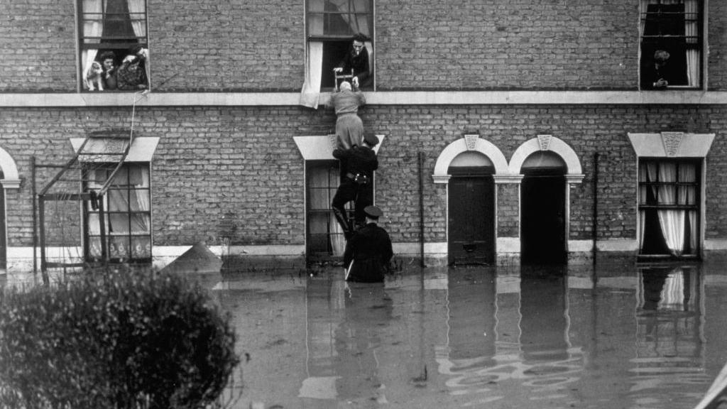 Firemen rescue inhabitants in Clapton, London, after the thaw from heavy snowfalls caused the river Lea to overflow its banks, flooding many houses and driving the occupiers into upstairs rooms.