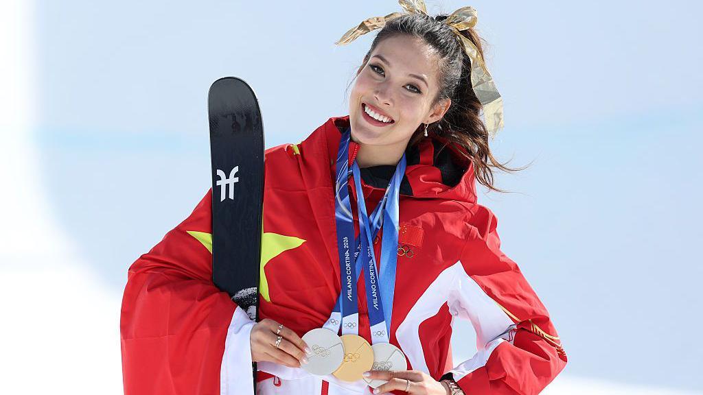 Eileen Gu poses while holding her three medals from the Milano Cortina 2026 Winter Olympics
