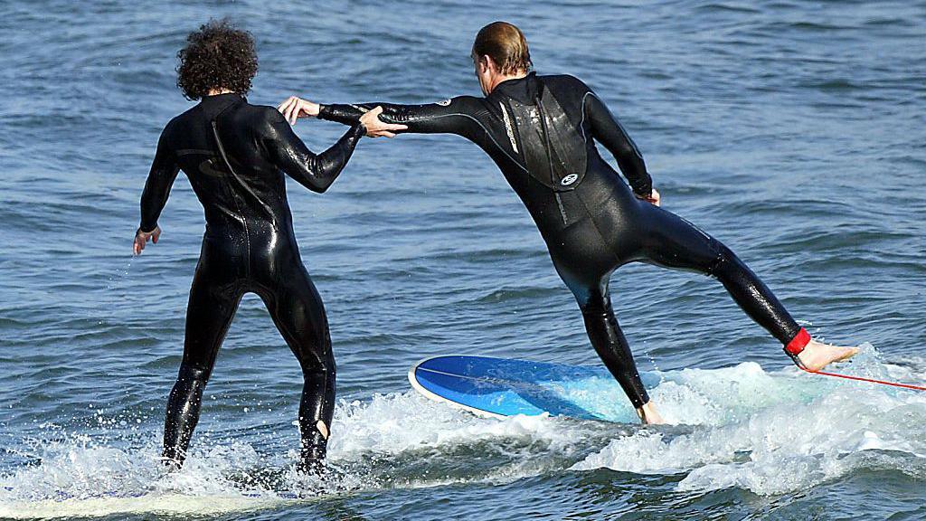 Two surfers in wetsuits ride boards in the Pacific Ocean