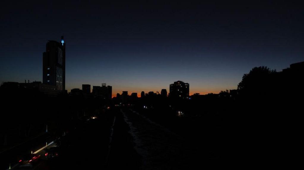 General view of Santiago, Chile, showing buildings in almost complete darkness silhouetted against an orange sunset.