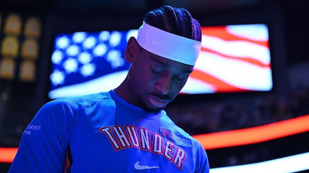 Shai Gilgeous-Alexander of Oklahoma City Thunder in a blue team leisurewear top and white headband, with his head bowed