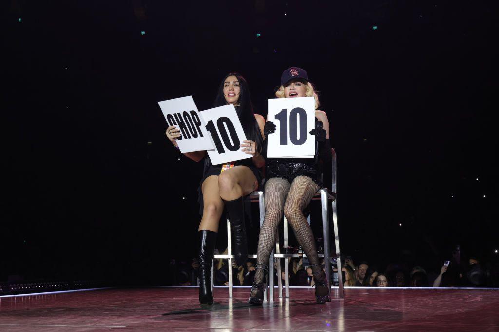 Madonna on stage with her daughter Lourdes in 2023. They are sitting on high stools, holding up score cards.