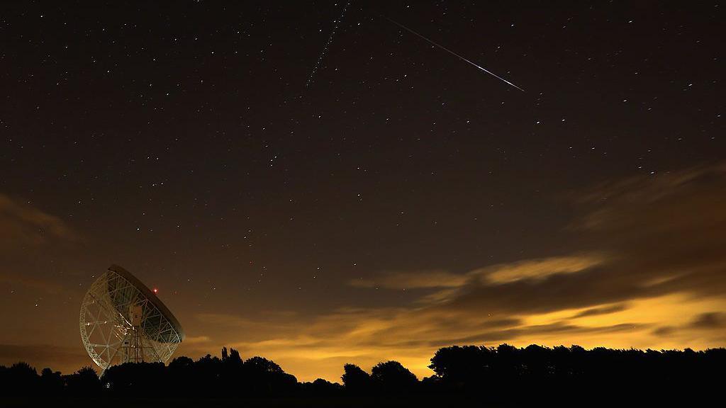 A Perseid meteor streaks across the sky over the Lovell Radio Telescope at Jodrell Bank.