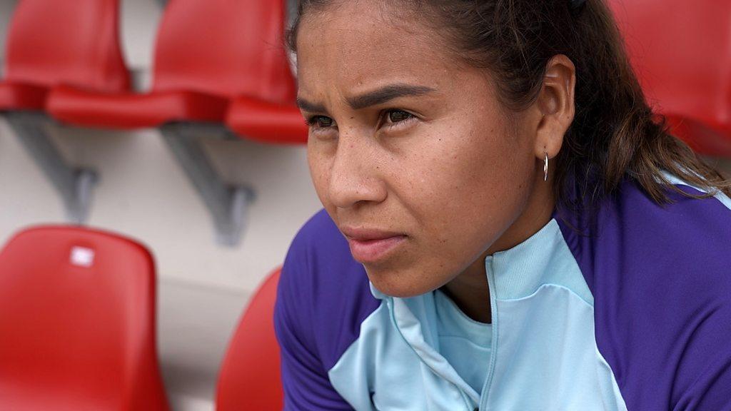 Leicy Santos sits leaning forward among stadium chairs as she looks out into the distance.