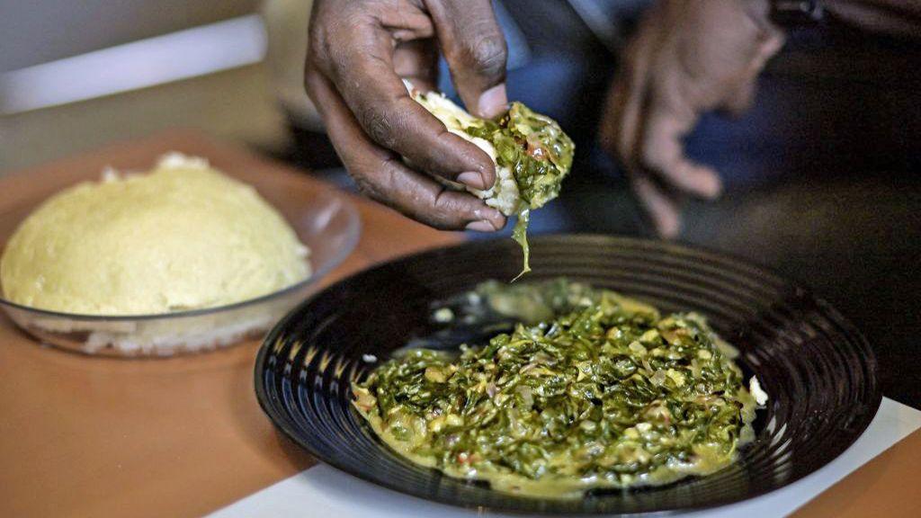 A chef tastes cooked maize meal alongside a vegetable dish