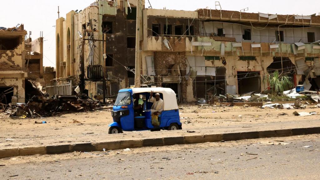 People drive pass damaged buildings in Khartoum