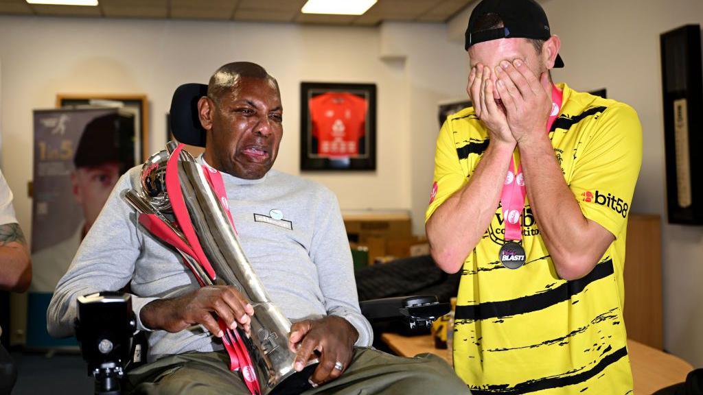 David Lawrence holding the T20 Blast trophy alongside James Bracey of Gloucestershire who is wearing a yellow shirt and putting his hands over his face with emotion