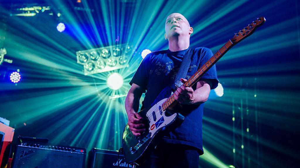 Stuart Braithwaite of Mogwai strums his guitar as a spotlight illuminates him from behind