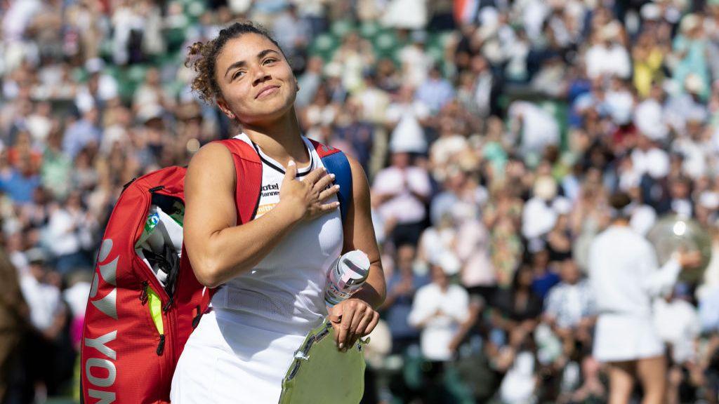 Jasmine Paolini smiles as she carries her tennis bag