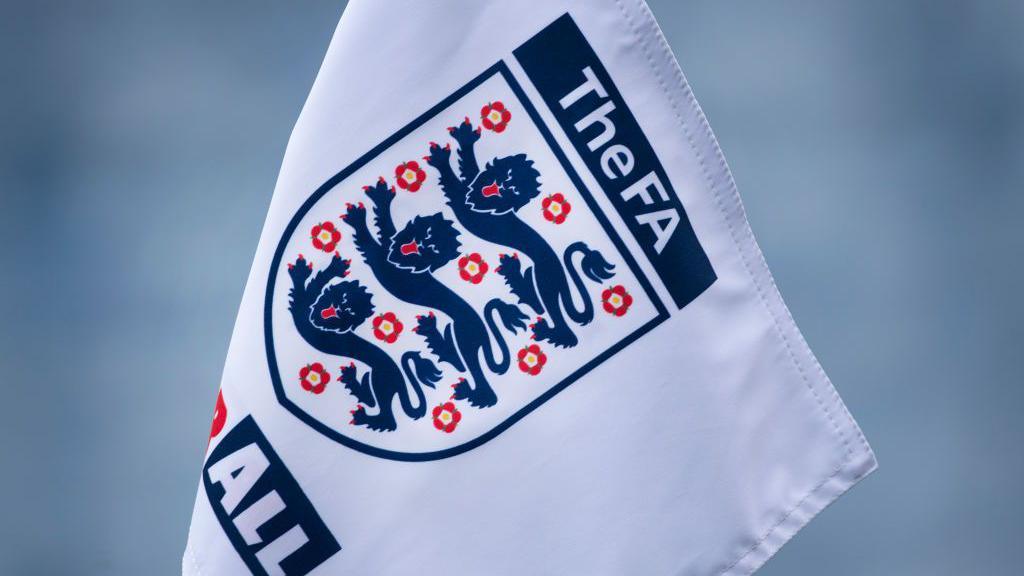 White flag featuring the FA logo - a blue shield outline featuing three horizontal blue lions and 10 small red roses