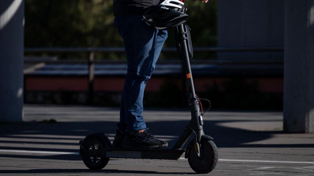 An individual riding an e-scooter on a road but can only be seen from the waist down