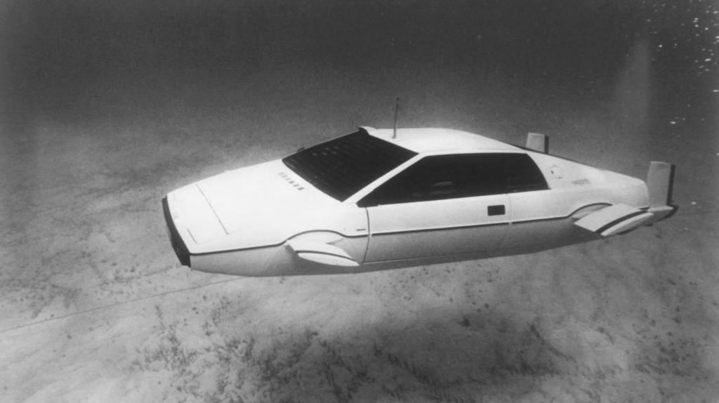 The Lotus Esprit car featured in the 1977 film The Spy Who Loved Me. The white car, featuring protruding fins on its sides and and propellers on its back, is floating underwater near the sea bed, in this black and white image.