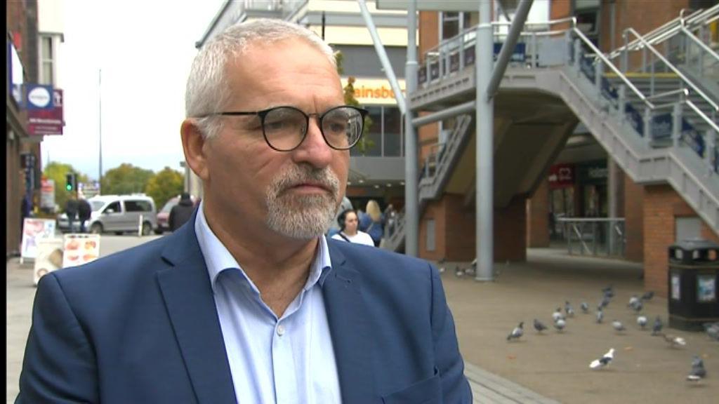 Richard Biggs, leader of Reigate and Banstead Council, wearing a blue jacke and shirt, standing in front of the closed Harlequin Theatre in Redhill.