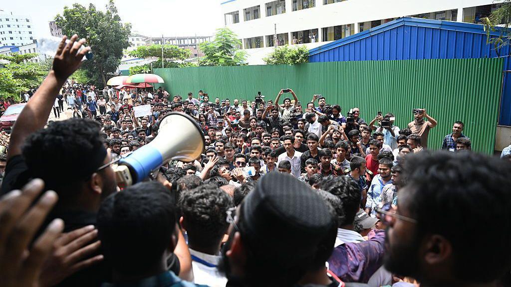 A man speaks into a megaphone in front of a crowd of protesters