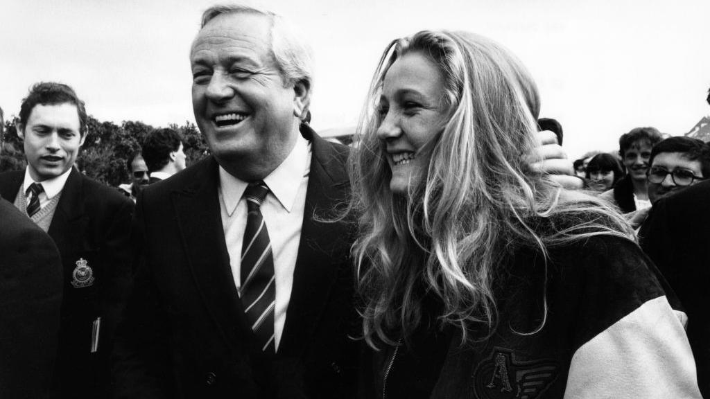 A woman and man in a suit and tie smile together in black and white