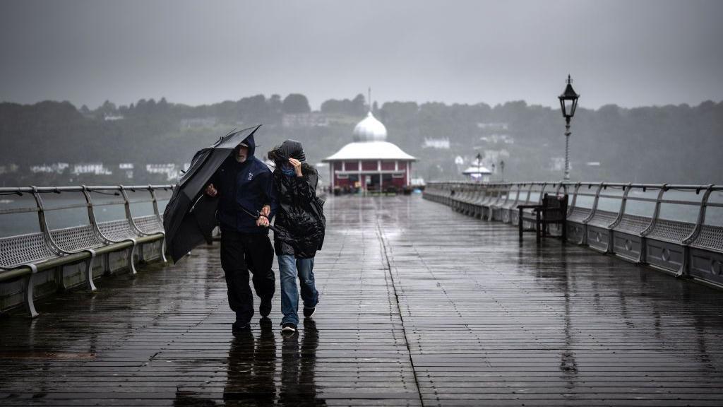 People walking along a pier with an umbrella on a wet and windy, grey day