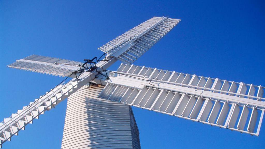 A general view of Thorpeness windmill in Suffolk. The angle of the picture looks up to the white coloured windmill and its large sails against a blue sky.