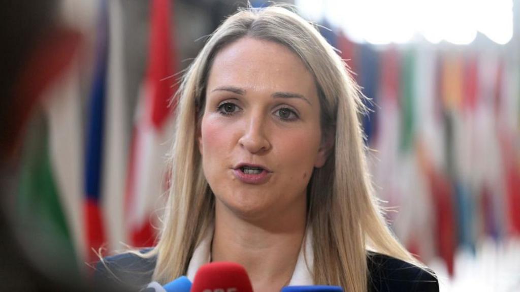 A woman with blonde hair talking to a red microphone