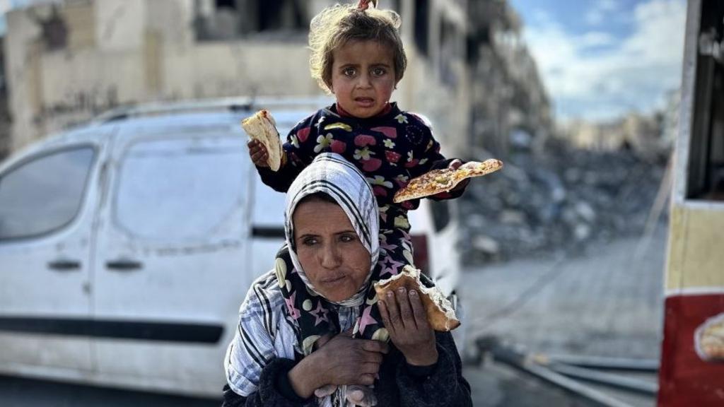 A child and a woman receive slices of free pizzas delivered from 34-year-old Palestinian chef Mohammed Al-Omrin at the pizza cart as Al-Omrin distributes free pizza to Palestinian children to those in need in Gaza City, Gaza on February 11, 2025.