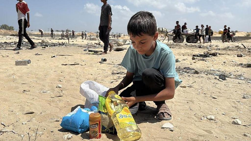 A boy is seen as Palestinians gather at the site where military cargo planes have dropped aid supplies from the air in the western part of Deir al-Balah, Gaza, on August 21, 2025.
