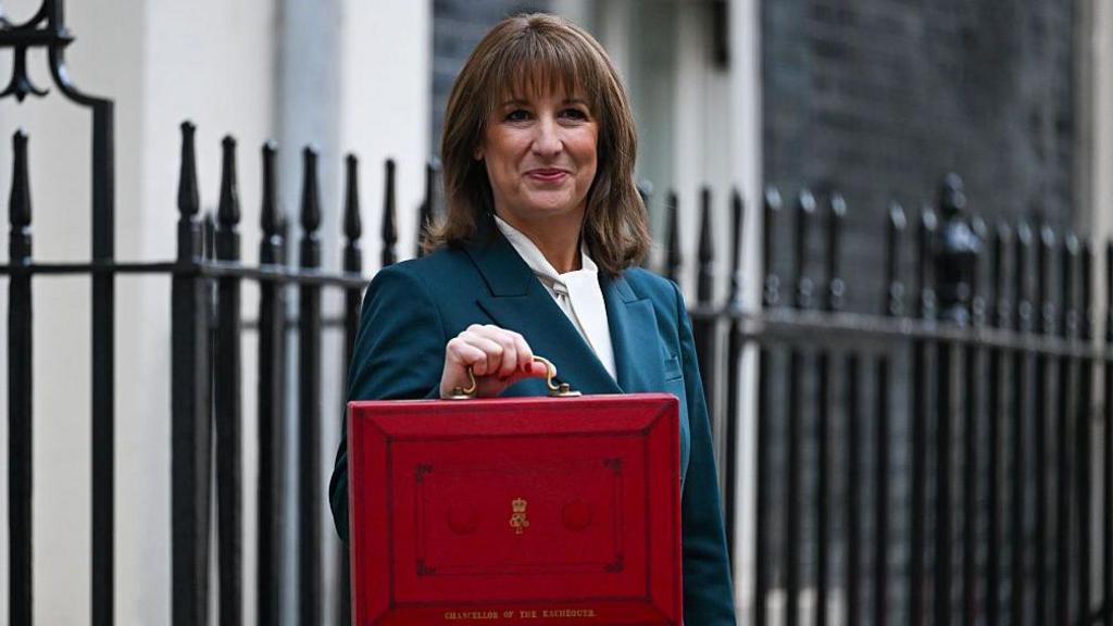 Rachel Reeves in a turquoise blazer and white shirt, holding a red briefcase.
