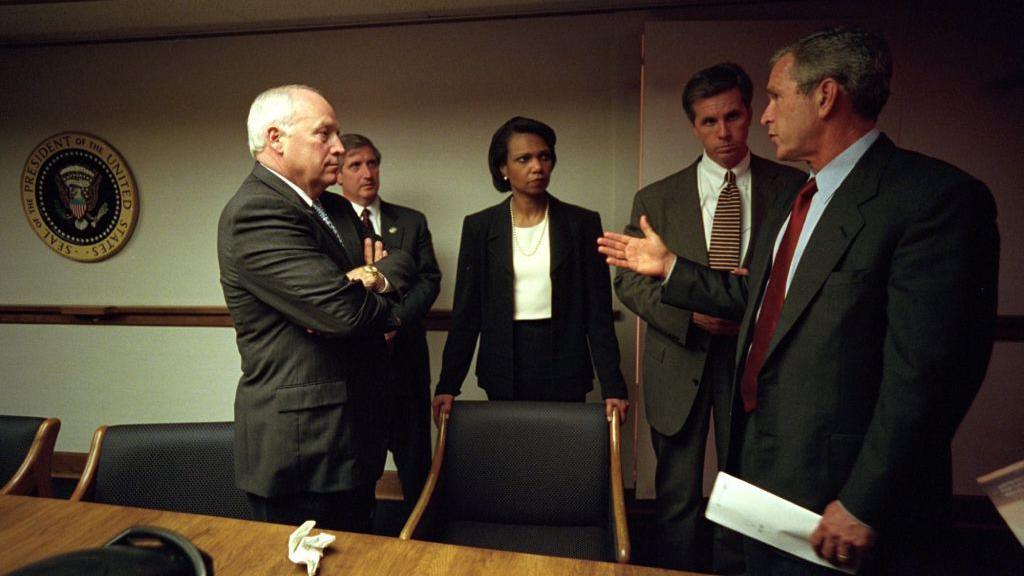 Cheney, Condoleezza Rice and George W Bush, as well as two other men, speaking in a board room