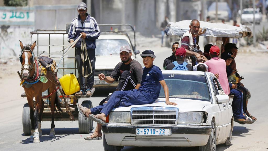 Groups of people sitting on cars and horse and cart along the road as they evacuate Deir al-Balah on 20 July