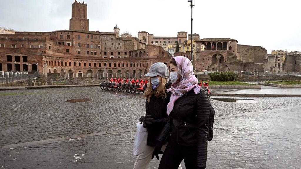 Two women wearing protective masks walks past the Trajan Forum in Rome on March 3, 2020