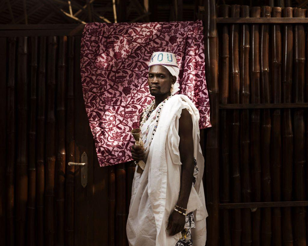 A man dressed in white poses for a portrait in a darkened room.