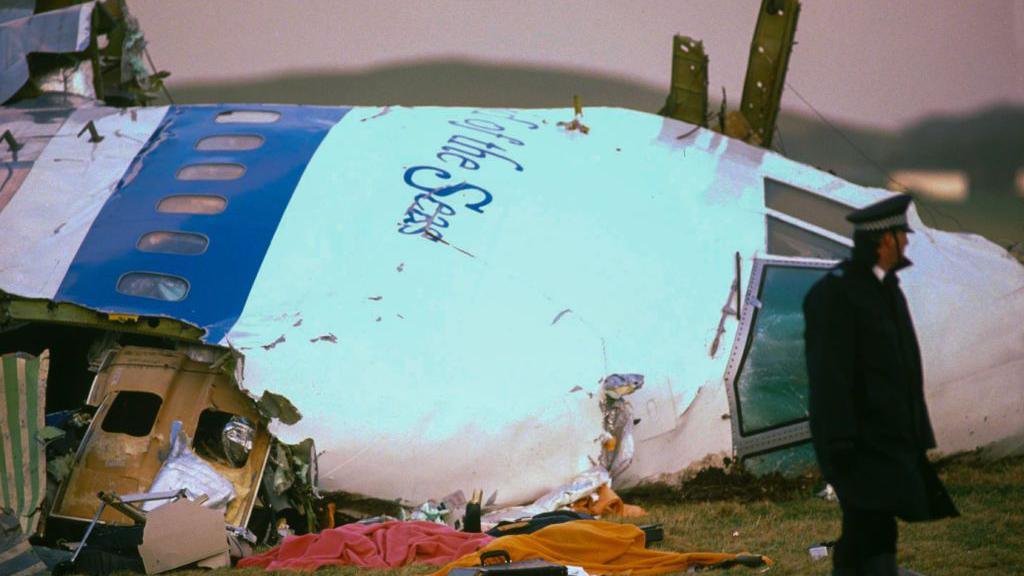 A uniformed police officer stands next to the destroyed cockpit of the plan after it exploded and landed in a field in Lockerbie