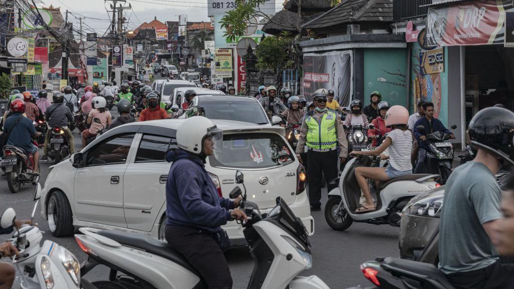 A road in Bali lined by shops, crowded with people on motorcycles and cars
