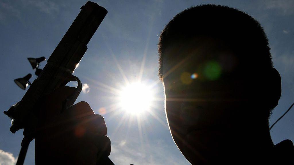 A silhouette of a young man holding a gun
