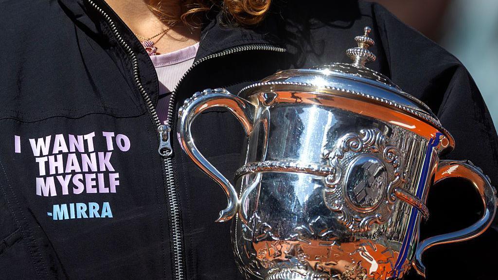 A close-up of Mirra Andreeva's jacket bearing the phrase 'I want to thank myself' while she holds the French Open winners' trophy
