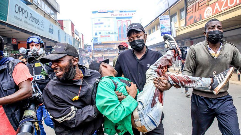 Angry youthful protesters help a man who was shot down during a demonstration over police killings of people protesting against Kenya's proposed finance bill in Nairobi  on 2 July 