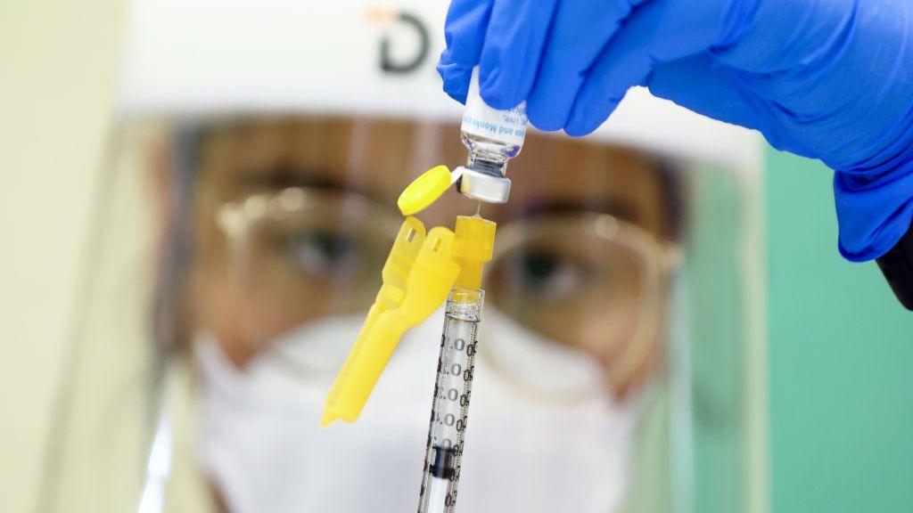 A nurse in protective gear holds a monkeypox vaccine