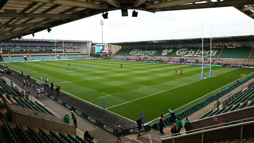 A mainly empty rugby stadium with a few people in the stands.  