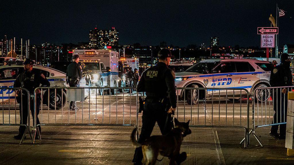 NYPD officer with a police dog and police cars in the background.
