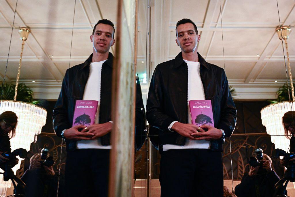 Rwandan-French writer and singer Gael Faye, whose image is also reflected in a mirror, poses with his book Jacaranda in Paris, France - Monday 4 November 2024