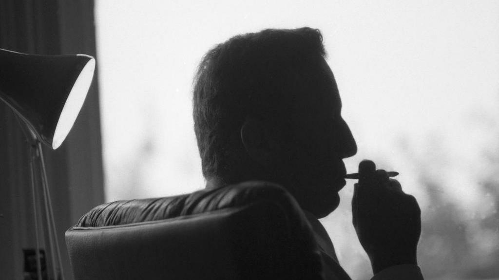 Frederick Forsyth is shown in silhouette while smoking.