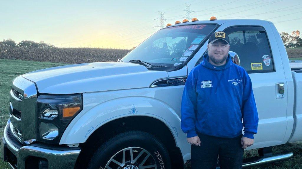 Ben Maurer wears a blue hoodie and black CAT baseball cap in front of a white pickup truck