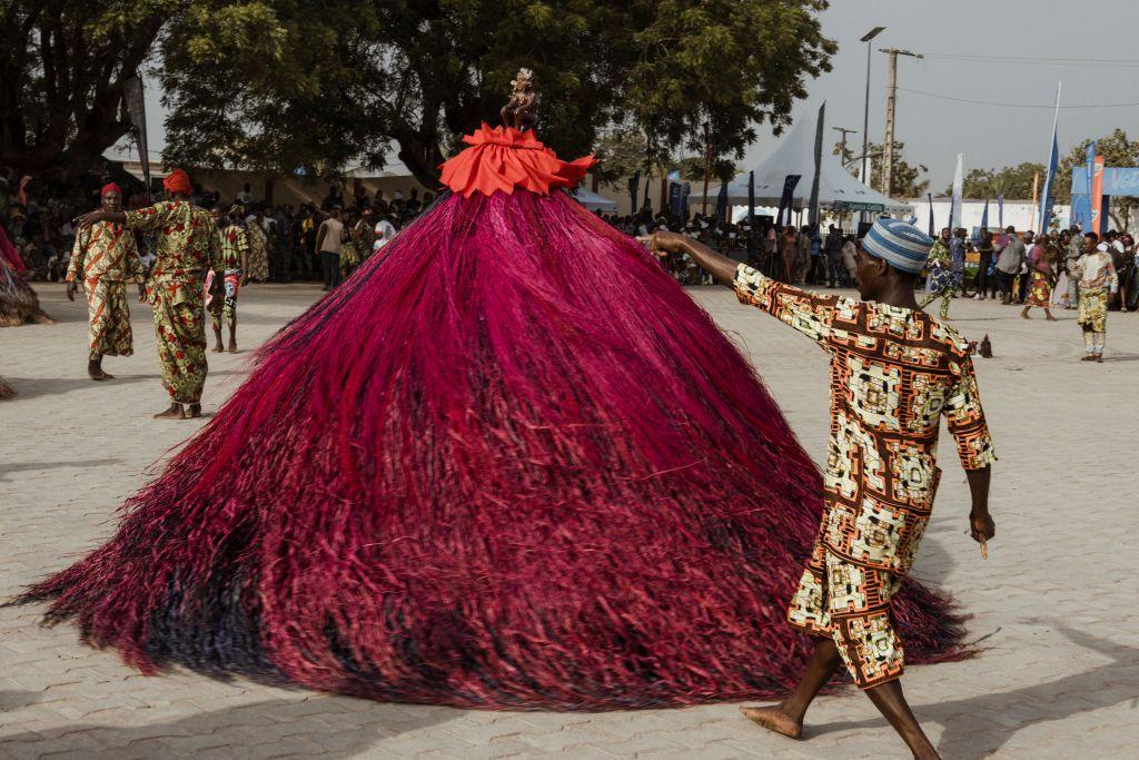 A person dances in circles wearing a huge swirling costume of long purple tassels,