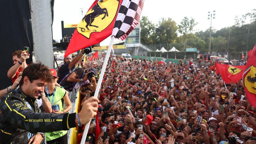 Charles Leclerc celebrates at the Italian Grand Prix last year by holding a Ferrari flag while fans raise their arms below