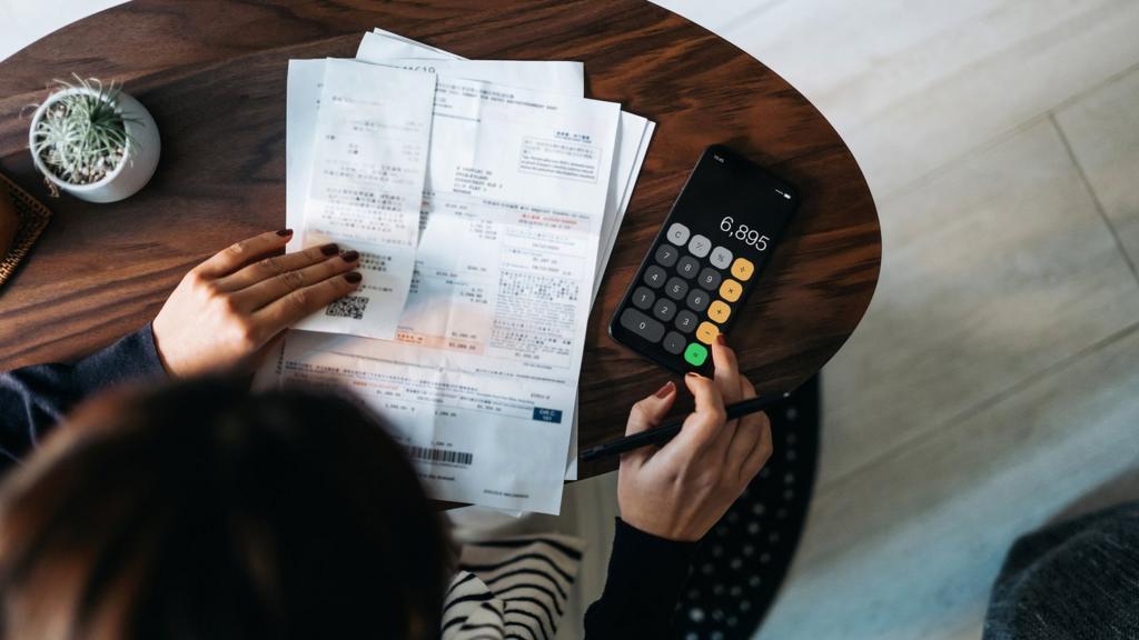 A high-angle view of a woman looking at her bills with a calculator