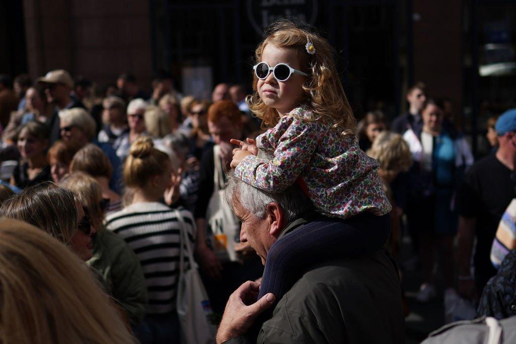 A young girl sits on the shoulders of a man as they wait to view the cortege carrying the coffin of the late Queen Elizabeth II on September 12, 2022 in Edinburgh, Scotland