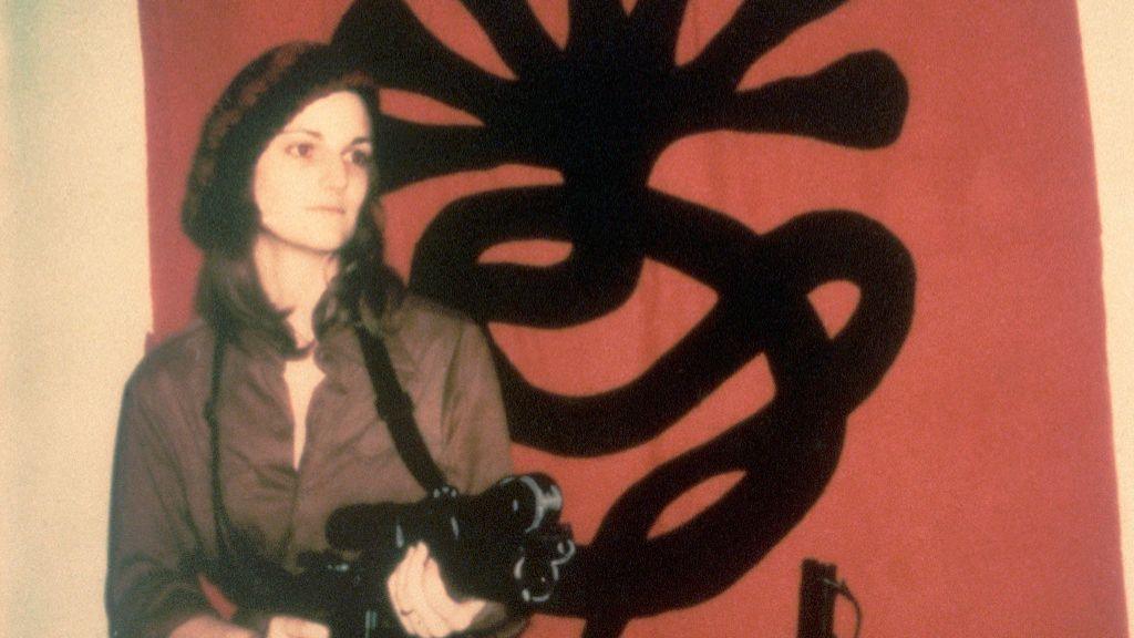 Portrait of American heiress Patty Hearst as she poses with a machine gun in front of a Symbionese Liberation Army flag, 1974