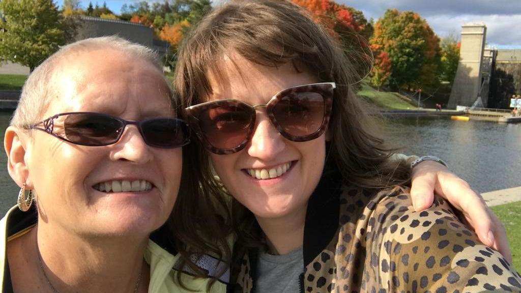 A selfie of Nichola Harris and her mother, both wearing sunglasses and smiling as they stand by a river