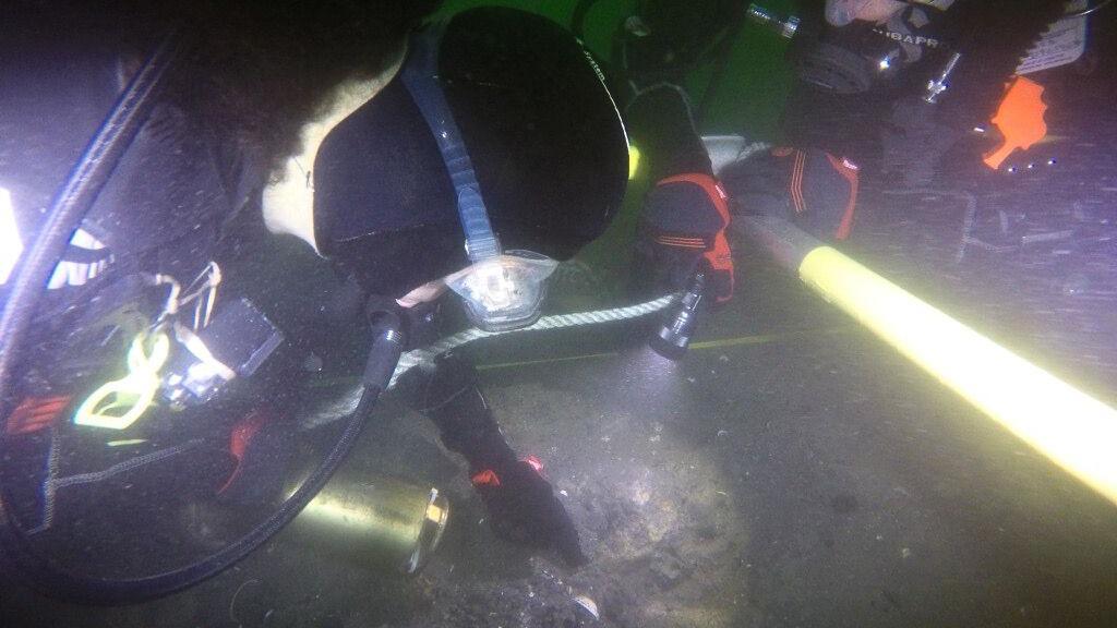 Divers with torches examine the underwater wreck.