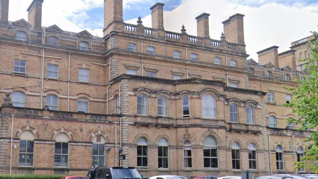 A wide hotel front with distinctive historic architecture. The top of some parked cars be seen in the foreground.