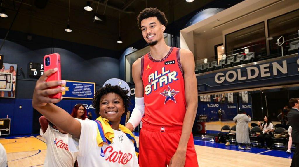 Victor Wembanyama poses with a fan for a selfie at all-star weekend